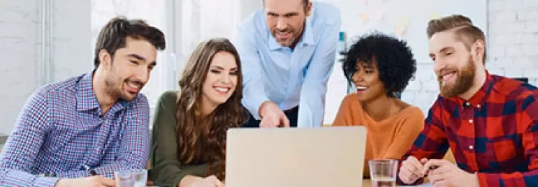 A group of people gathered around a laptop in a bright office.