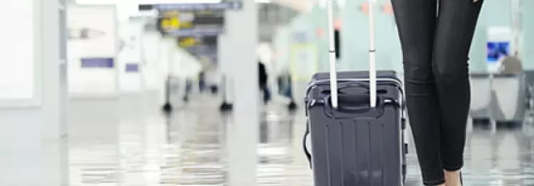 Person walking in an airport with a rolling suitcase.