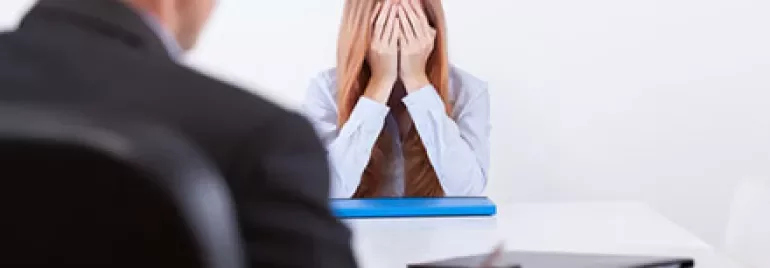Person at a desk with hands covering face, another sitting nearby.