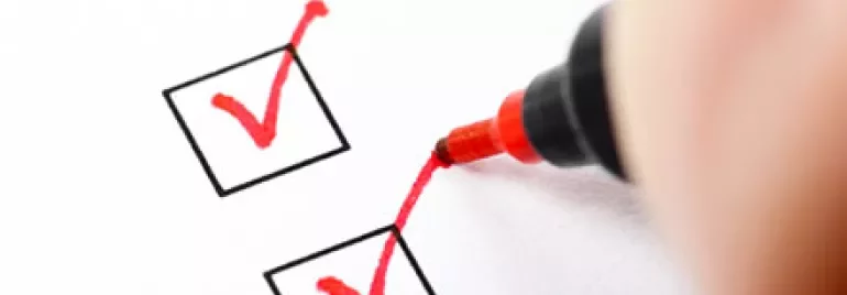 Close-up of a red pen ticking checkboxes on paper.