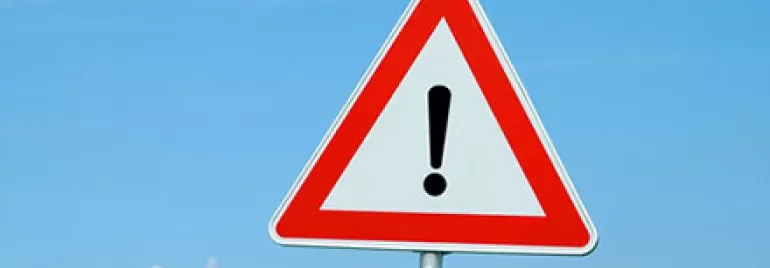 Triangular warning sign with exclamation mark against a blue sky.