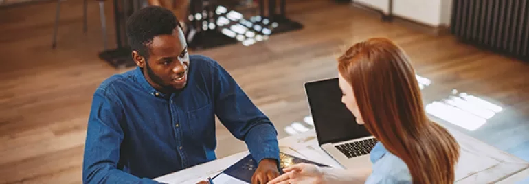 Two people discussing paperwork at a table with a laptop.