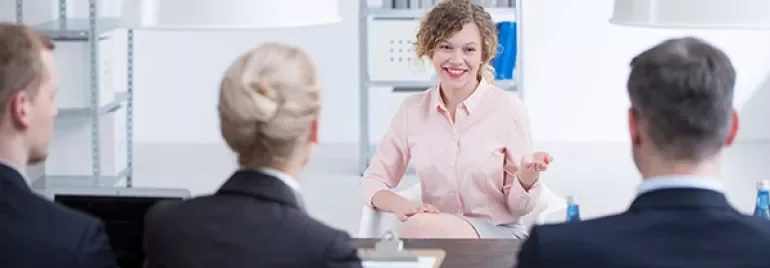Person smiling during an interview, seated across a table from three people in an office setting.