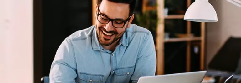 Person smiling while working on a laptop in a cozy office.
