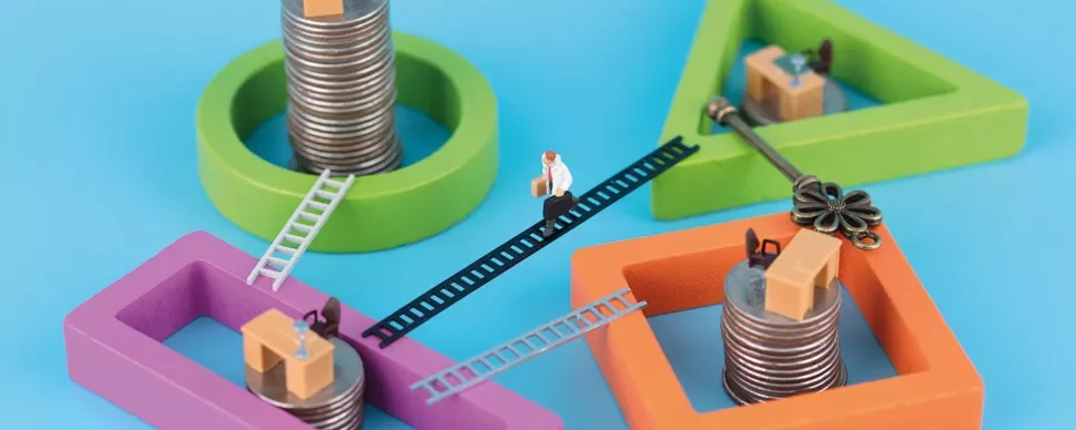 Miniature person walking on coins and gears with wooden shapes and ladders.