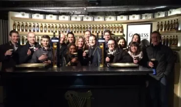 Group enjoying drinks at a brewery with bottles displayed behind them.