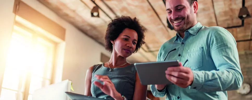 Two people looking at a tablet in a bright office setting.