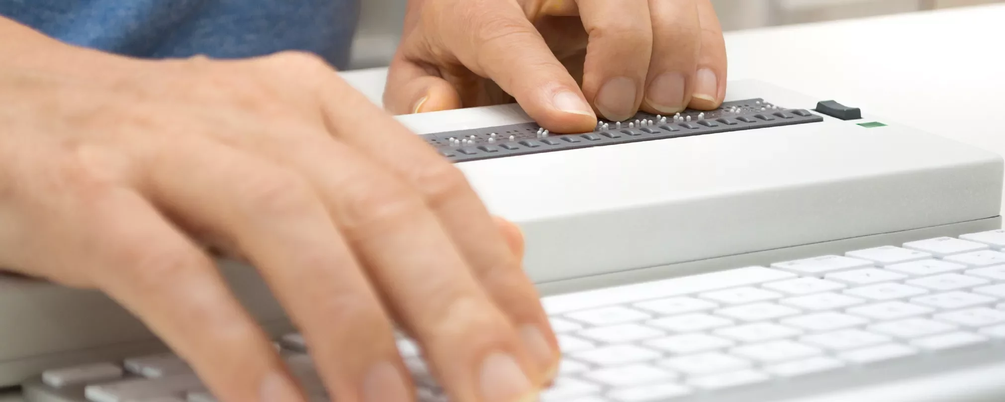 Hands using a Braille display and a keyboard.