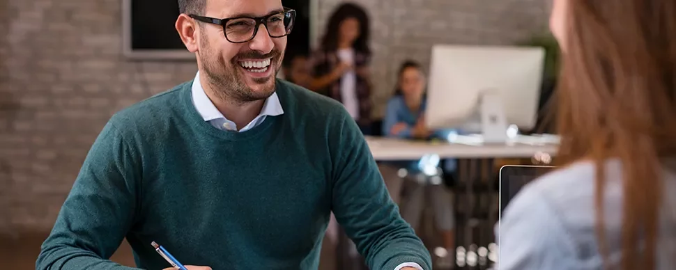 Person smiling during a conversation at a desk in an office.