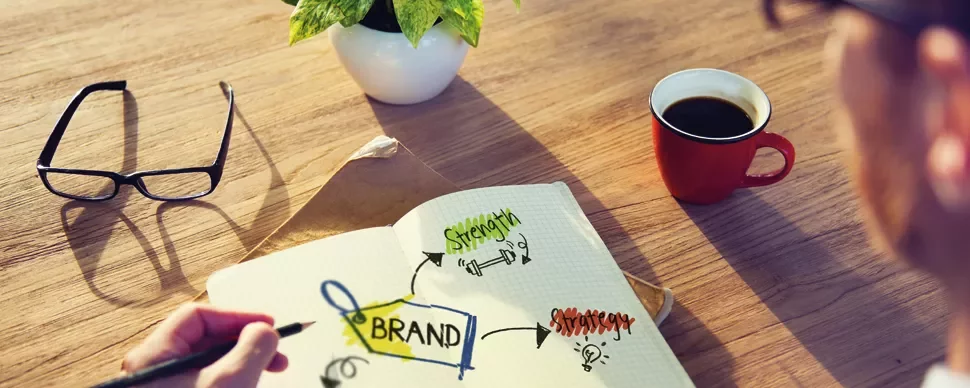 Person brainstorming brand strategy with coffee and notebook.