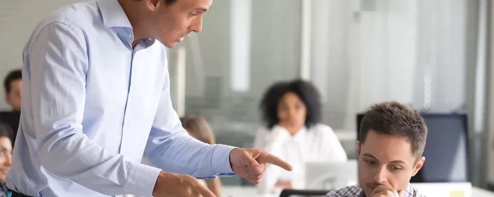 Person in a blue shirt speaking to a thoughtful colleague in an office.