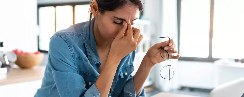 Person holding glasses and rubbing eyes in a bright room.