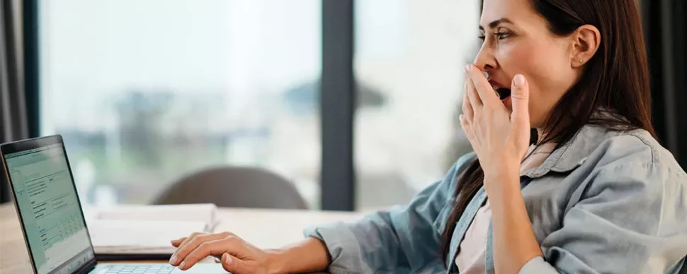Person at a desk yawning while using a laptop.