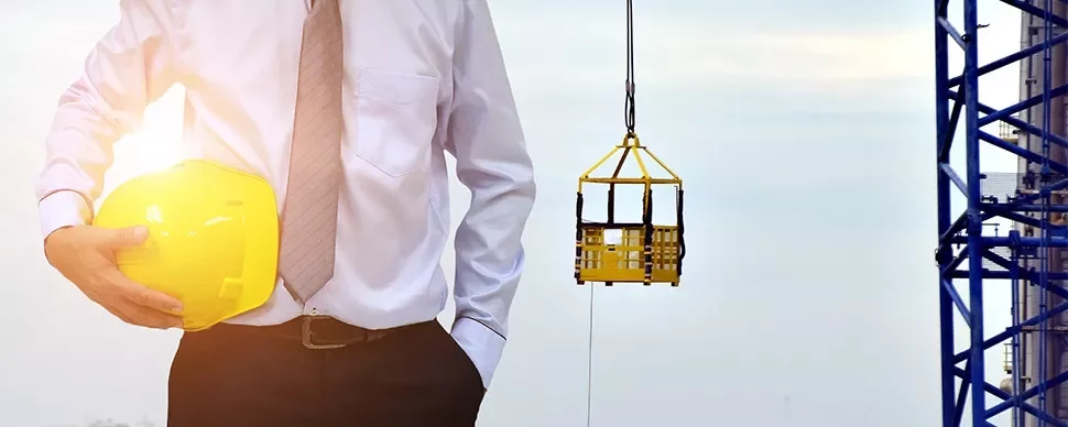 Person holding a yellow hard hat at a construction site with a crane in the background.