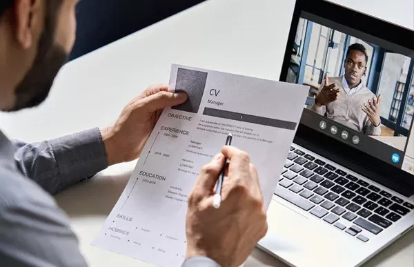 Person reviewing CV during online job interview with video call on laptop.