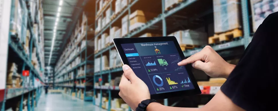Person using a tablet with warehouse management software in a large storage facility.