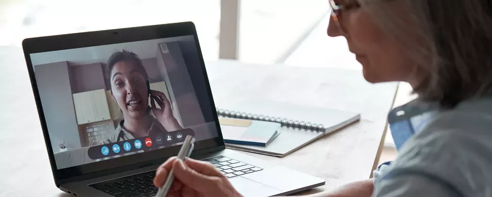 Person on a video call using a laptop, taking notes with a pen.