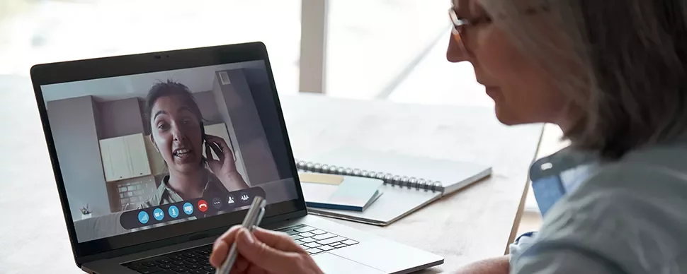 Person on a video call using a laptop, with a notebook and pen on the table.