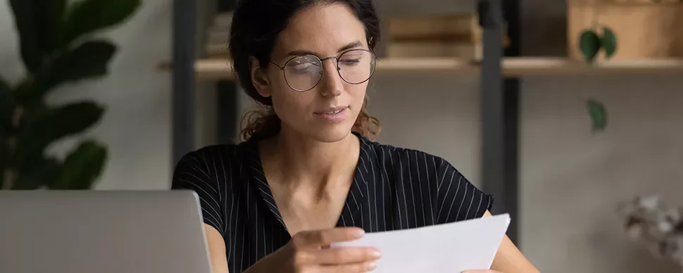 Person wearing glasses focused on reading a document at a desk.