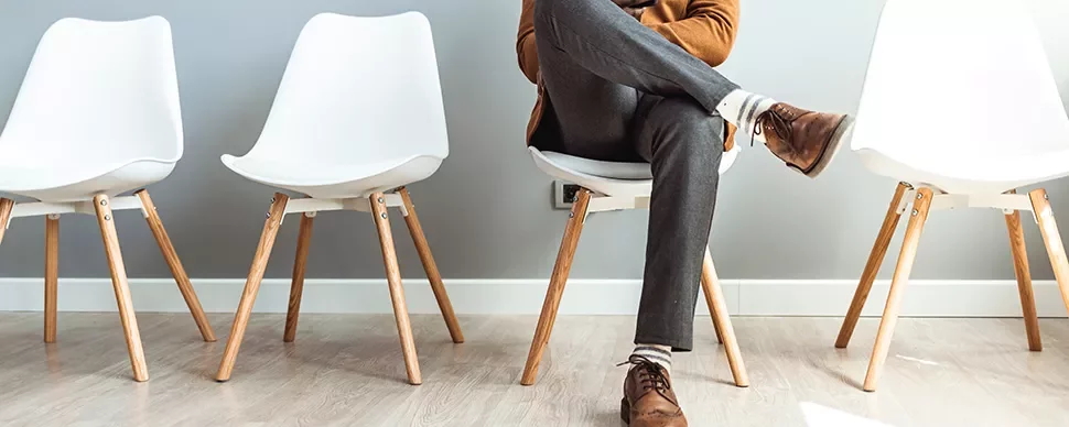 Person sitting on a chair with legs crossed, between two empty chairs in a modern room.