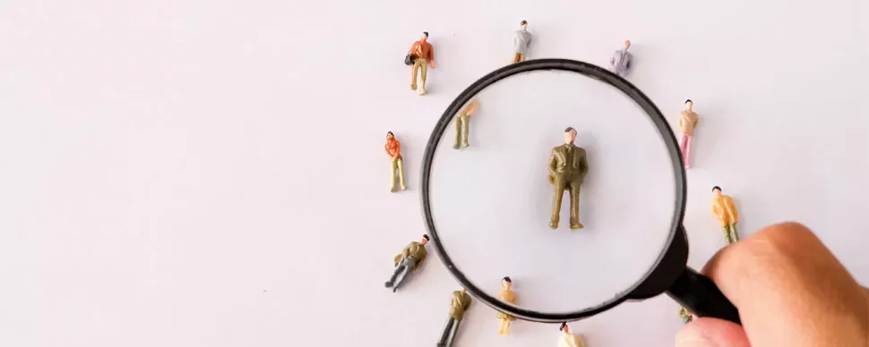 Magnifying glass focusing on a small figurine among several others on a white background.