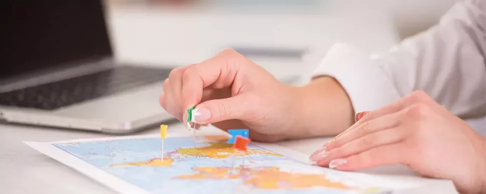 Person placing pins on a map next to a laptop.