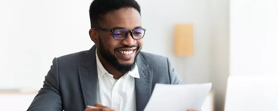 Person in a suit smiling while reading a document.