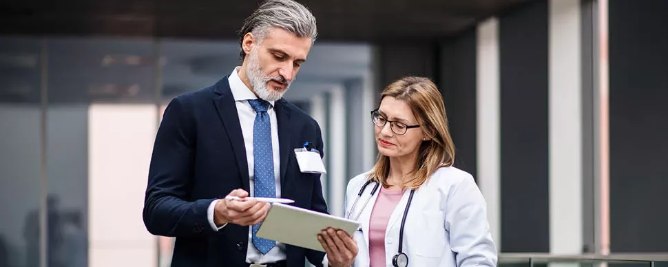 Two professionals discussing information on a clipboard in an office setting.