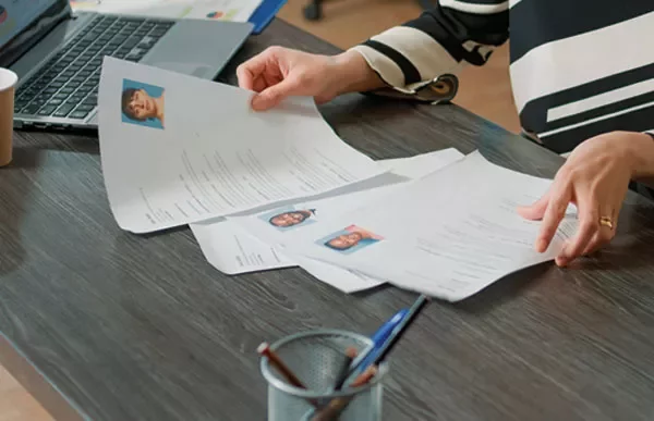 Person sorting through resumes at a desk with a laptop and pens.