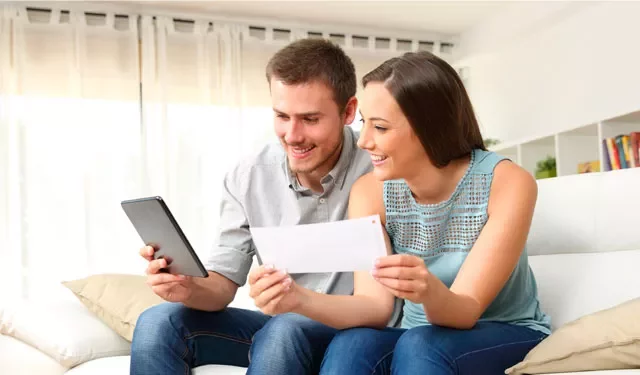 Two people smiling while looking at a tablet and a paper.