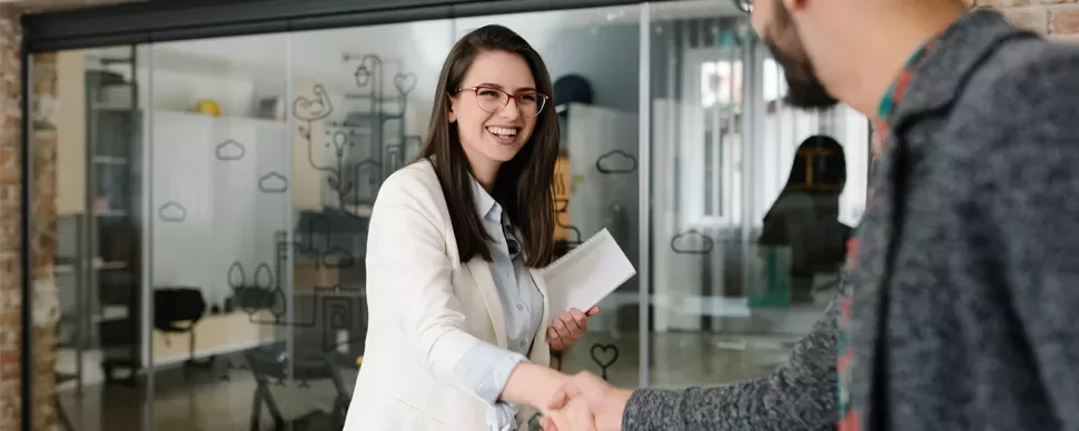 Two people shaking hands in an office with glass walls
