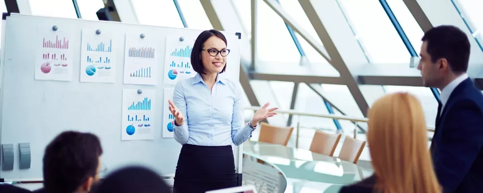 Person giving a presentation with charts on a whiteboard in a modern conference room.
