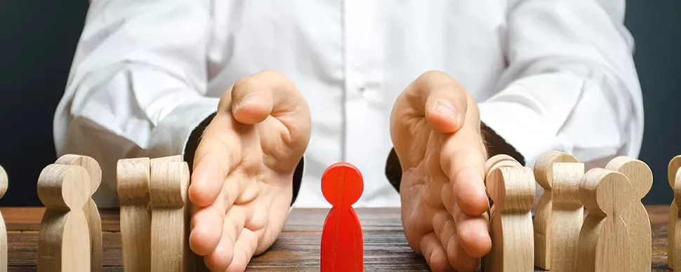 Hands separating a red figure from wooden figures on a table.