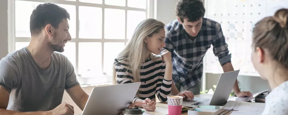Group of people collaborating in a bright office with laptops.