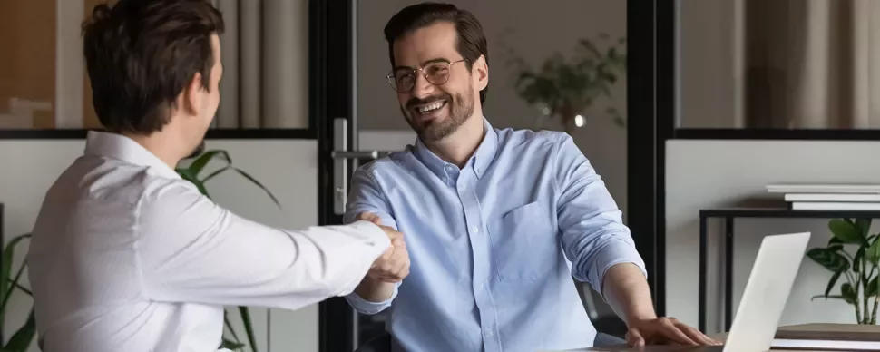 Two people smiling and shaking hands in an office setting.