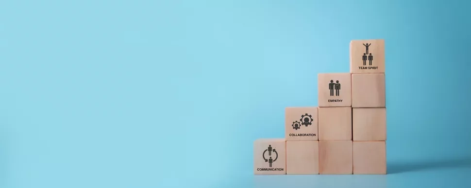 Wooden blocks stacked on blue background symbolizing communication, collaboration, empathy, and team spirit.