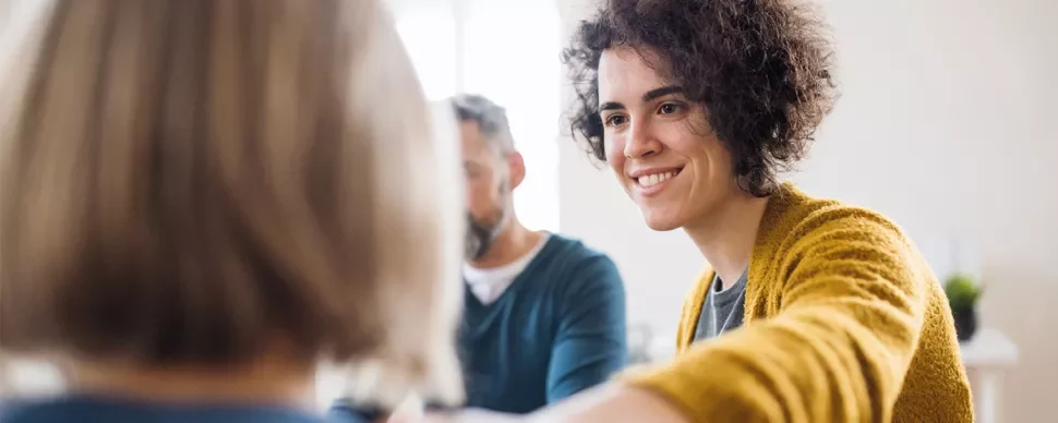 Person in yellow sweater smiling and interacting in a group discussion.
