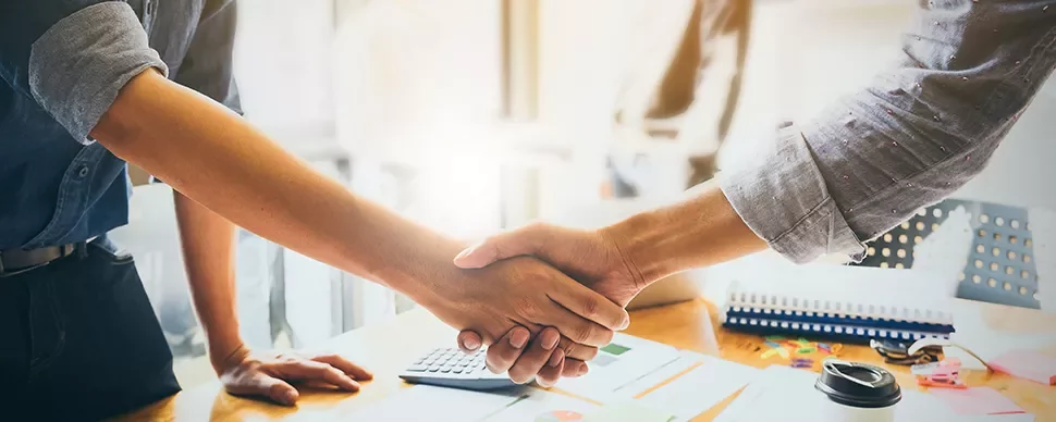 Two people shaking hands over a desk.