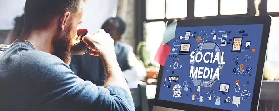 Person sipping coffee in front of a computer screen displaying social media icons.