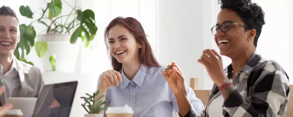 Three people sitting at a table, smiling and laughing during a meeting.