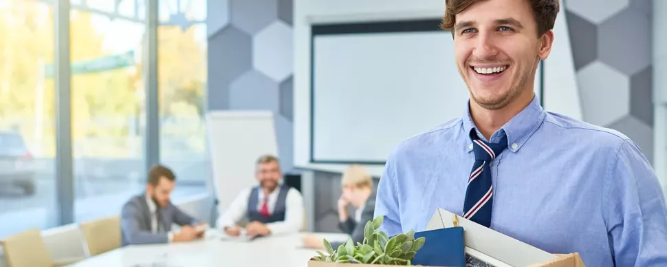 Person in office holding a box with colleagues in the background.