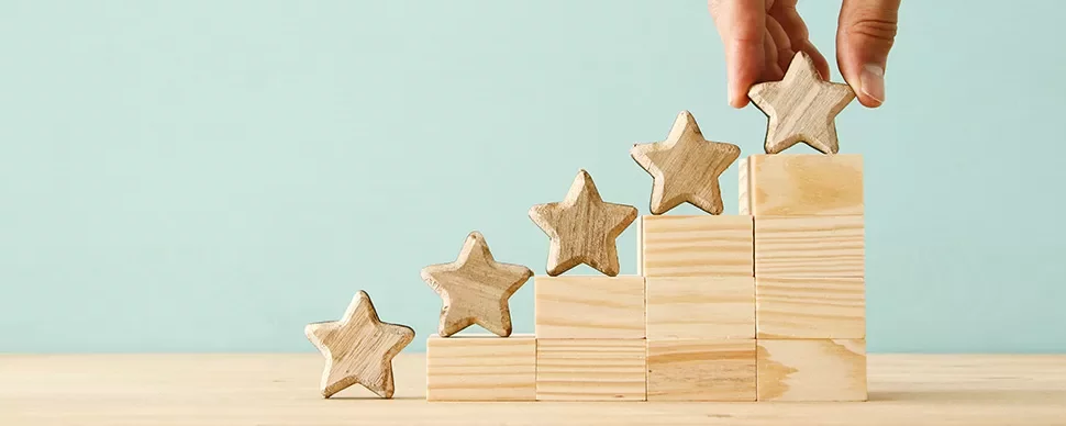 Hand placing wooden star on blocks arranged in steps.