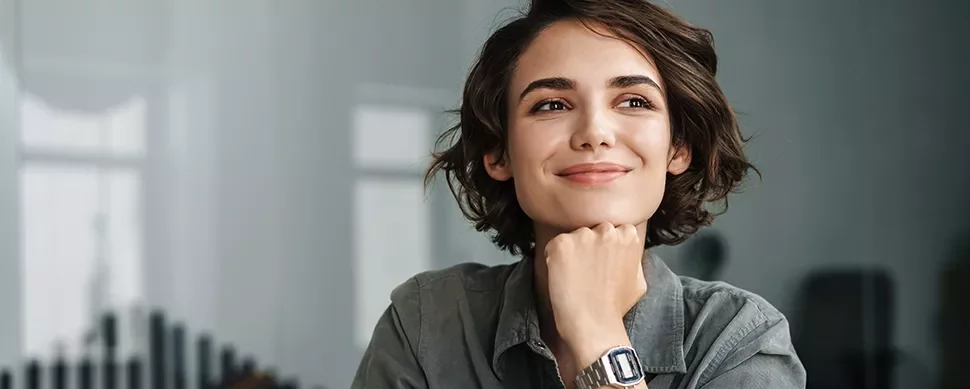 Person with short hair smiling, wearing a wristwatch, thoughtful pose.