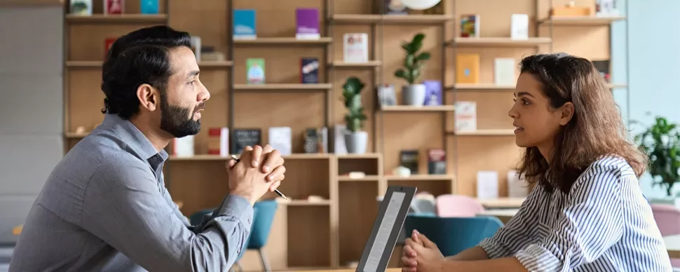 Two people sitting at a desk having a conversation.