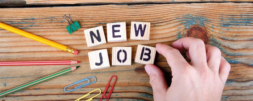 Wooden blocks spell 'New Job' on a wooden surface with office supplies nearby.