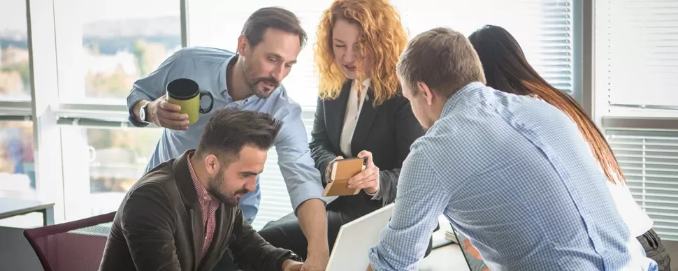 Group of people collaborating around a laptop in an office.