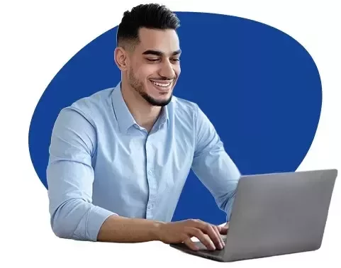 A man with a blue long sleeve shirt, sitting and smiling in front of a laptop with a blue background
