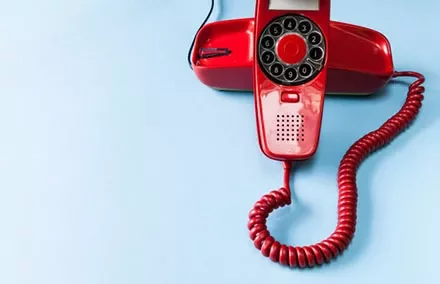 Red rotary phone on a light blue background.