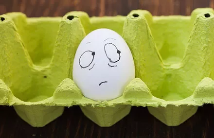 A white egg with a drawn face showing a worried expression in a green egg carton.