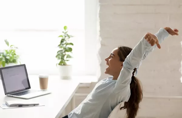Person stretching at a desk with a laptop and coffee cup.